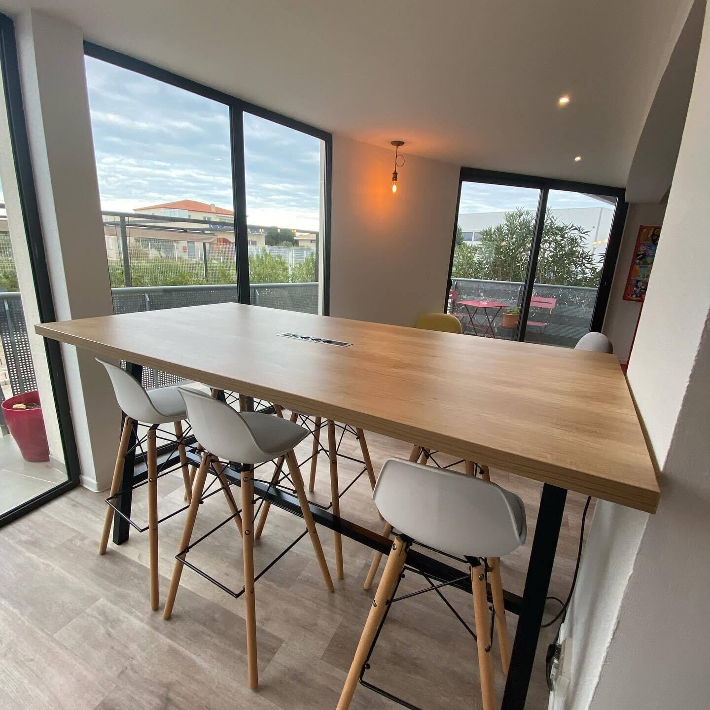 A modern dining area with a long wooden table, four white chairs, and large windows offering views of buildings and greenery.
