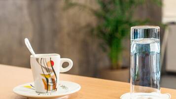 A cup with a spoon on a saucer, a glass of water, and a pen on a table.