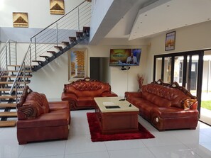 A spacious living room with a staircase, leather sofas, a coffee table, and a flat-screen TV. - Avalon Lodge (East London)