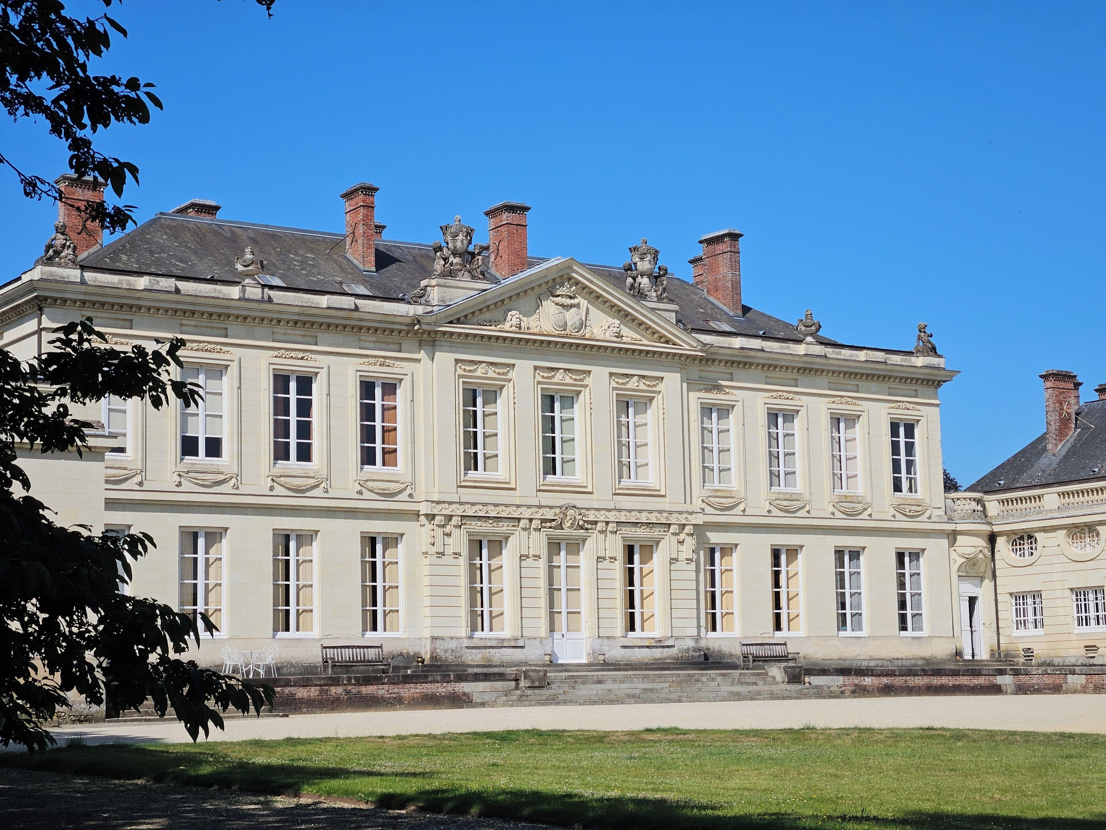 A large, historic building with symmetrical architecture, multiple chimneys, and a central entrance with steps.