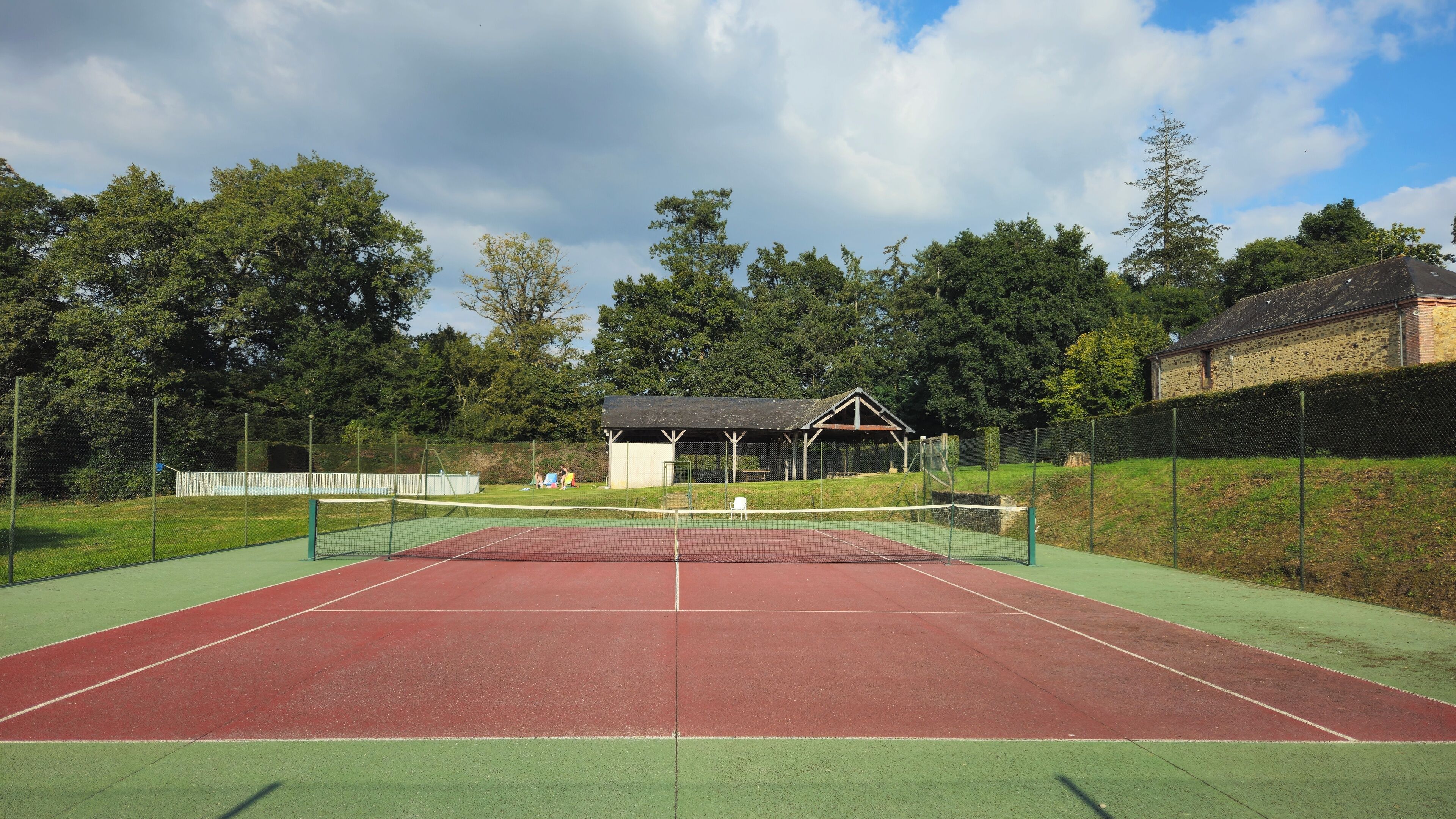 Un court de tennis en plein air, doté d’une zone de sièges abritée et d’un bâtiment en arrière-plan.