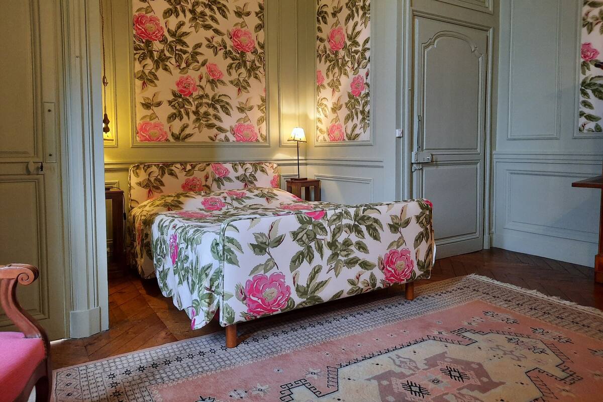 A bedroom with a floral bedspread, a wooden chair, a nightstand, and a patterned rug.