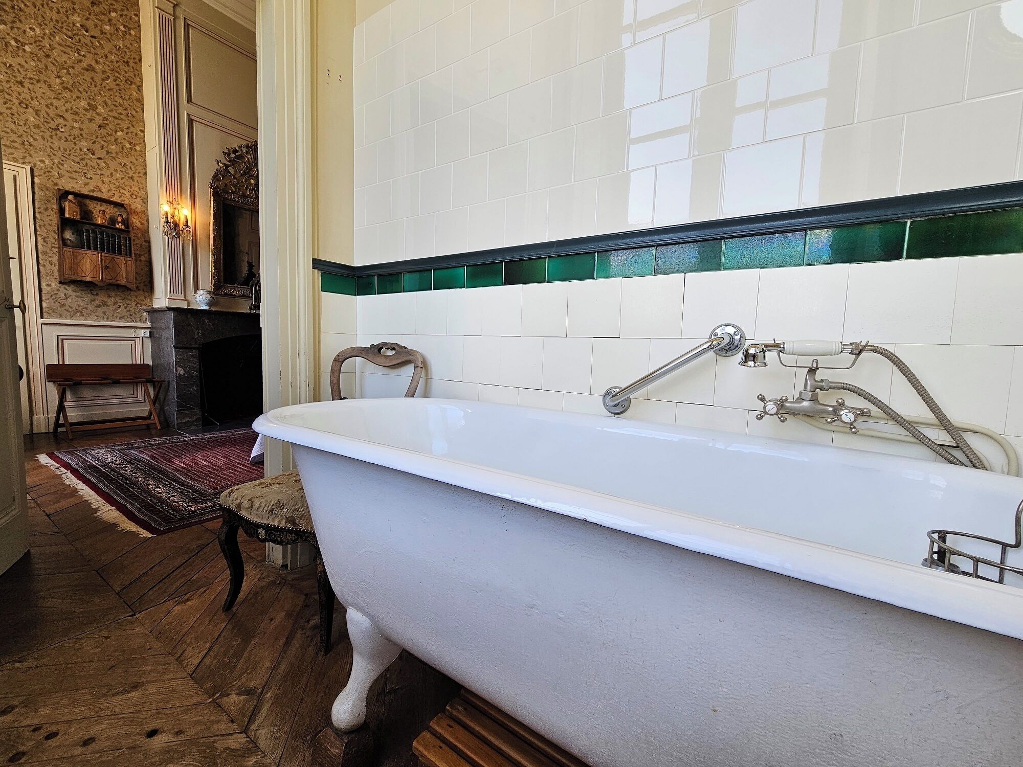 A bathroom with a freestanding bathtub, a wooden bench, a patterned rug, and a tiled wall with a green border.