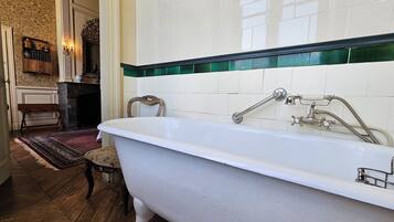 A bathroom with a freestanding bathtub, a wooden bench, a patterned rug, and a tiled wall with a green border.