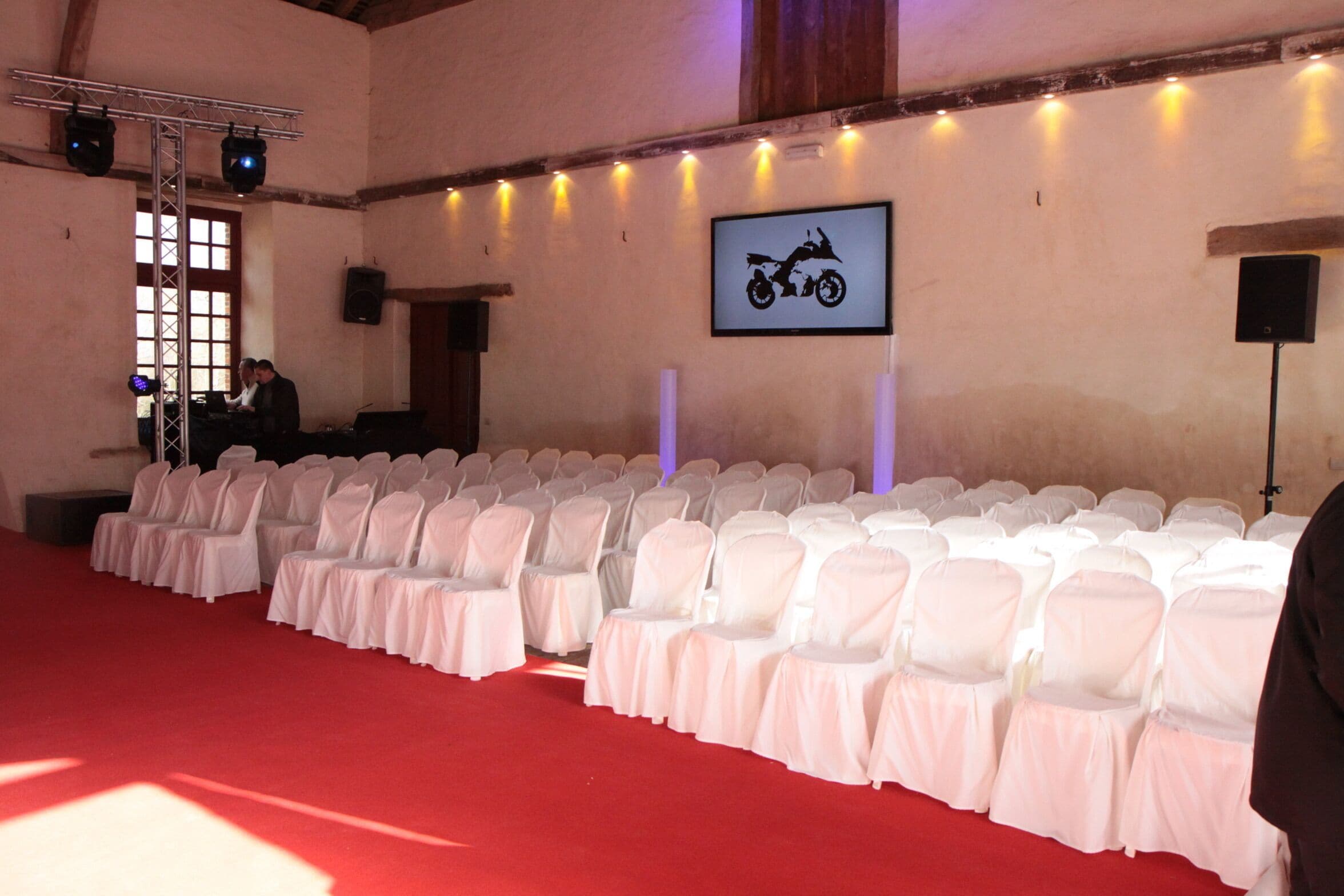 A conference room with rows of white chairs, a red carpet, and a motorcycle-themed wall decoration.