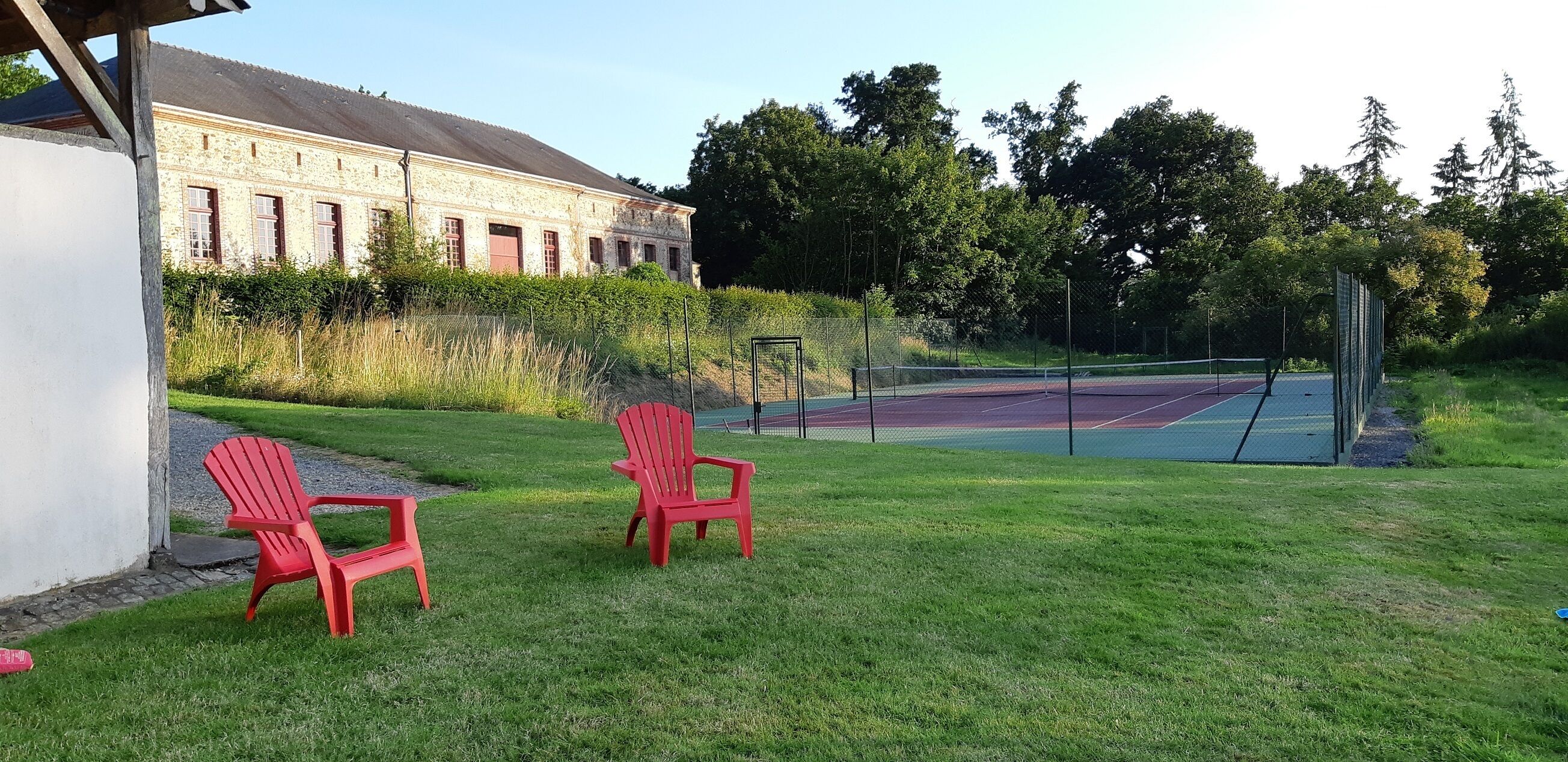 Un court de tennis avec deux chaises rouges et un bâtiment en arrière-plan.
