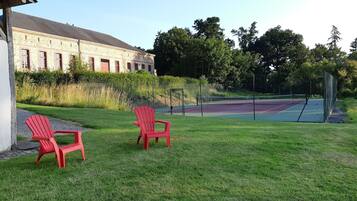 Un court de tennis avec deux chaises rouges et un bâtiment en arrière-plan.