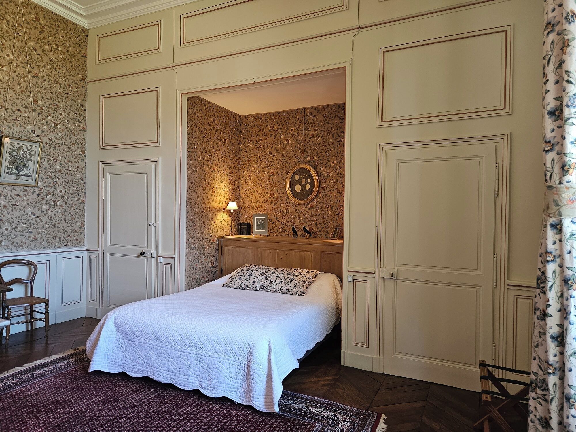 A bedroom with a bed, a nightstand, a mirror, and a door leading to another room.