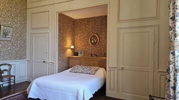 A bedroom with a bed, a nightstand, a mirror, and a door leading to another room.