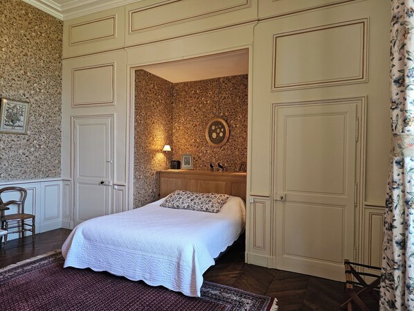 A bedroom with a bed, a nightstand, a mirror, and a door leading to another room. - Chateau de Craon (Craon)