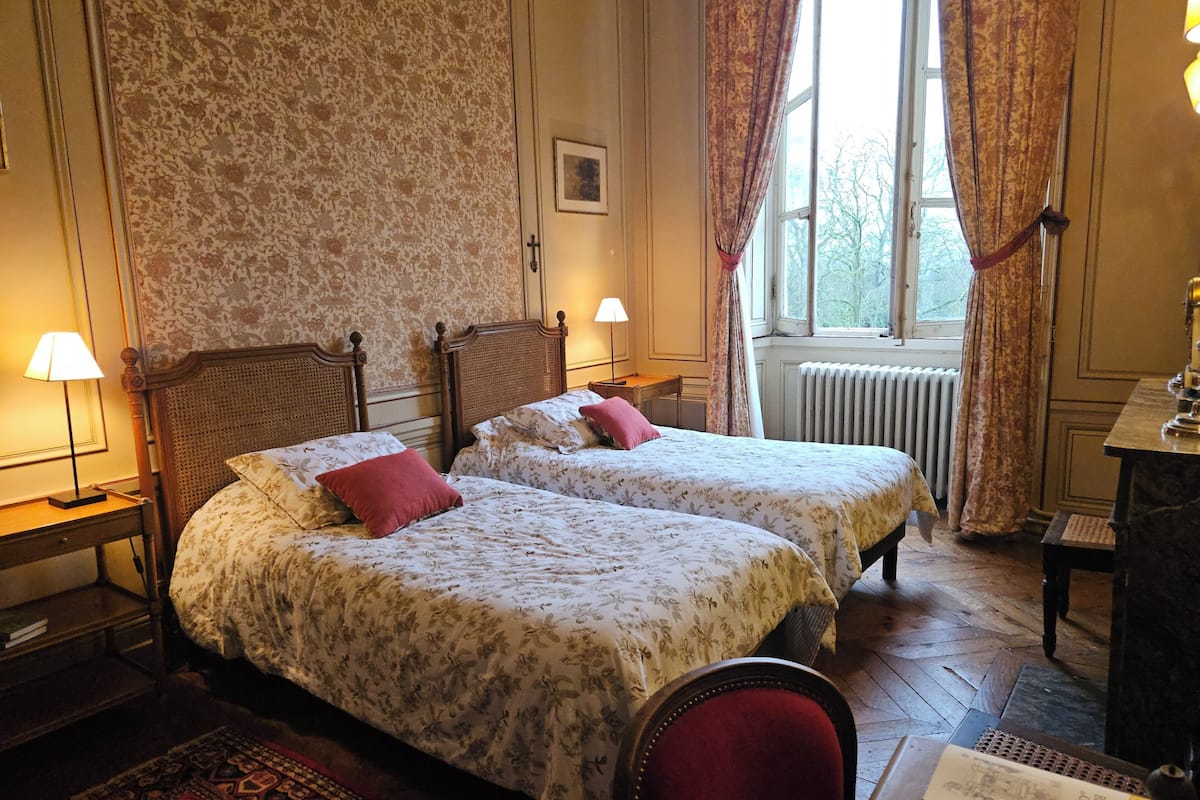 A traditional room with two single beds, a wooden floor, a radiator, and a desk with a lamp.