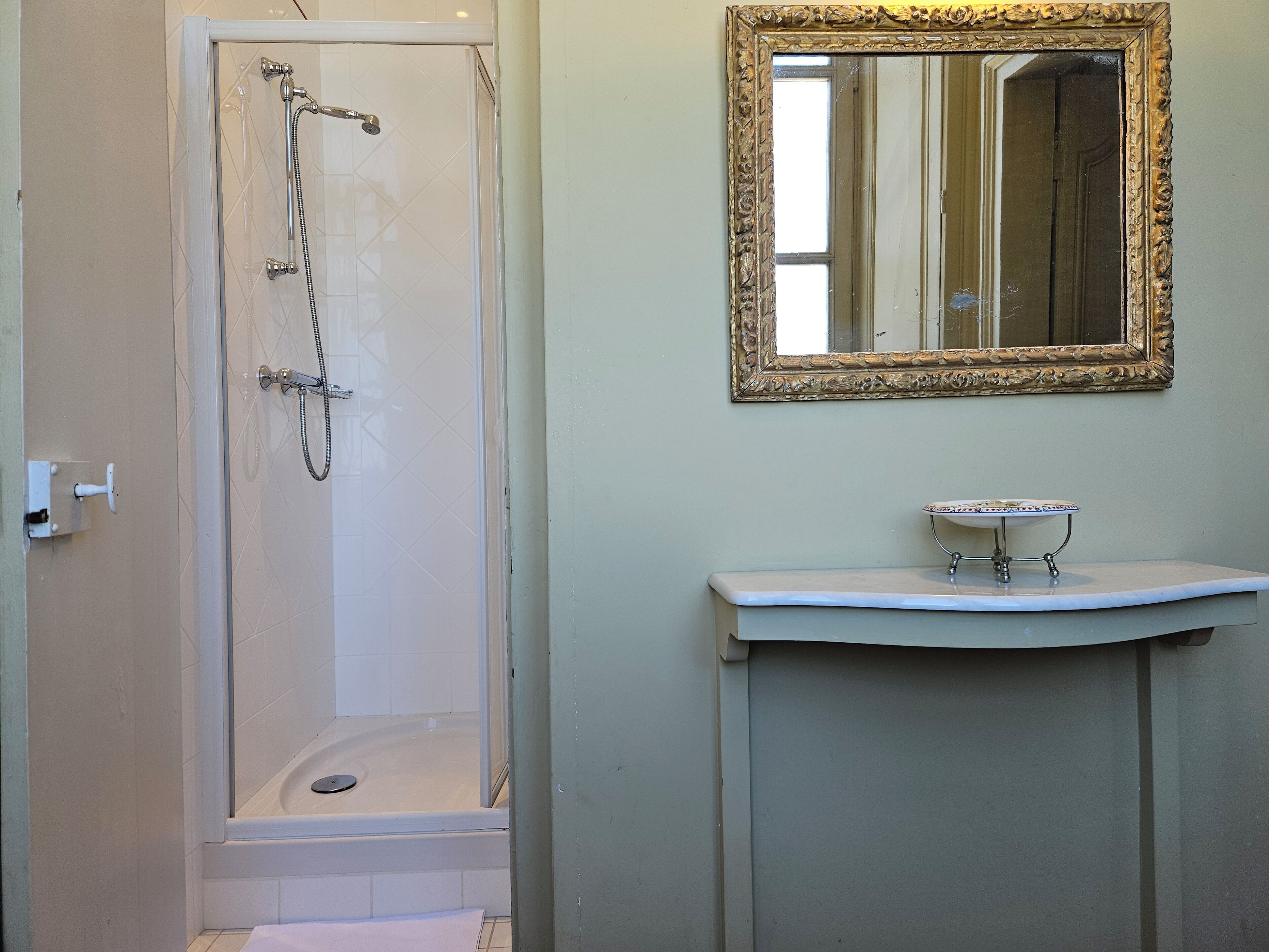 Un baño con ducha de vidrio, un lavabo con una pila decorativa y un espejo con un marco ornamentado.