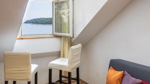 Une pièce avec un plafond en pente, une fenêtre donnant sur un plan d’eau, deux chaises et un canapé avec des coussins.