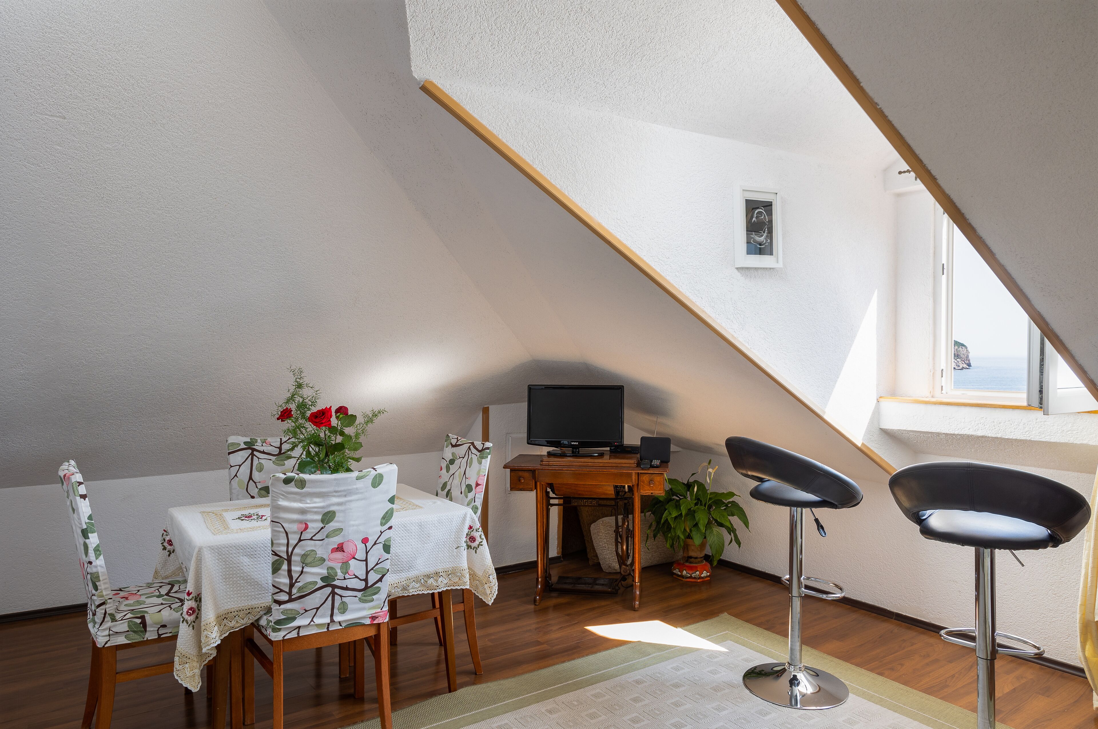 A cozy attic room with a dining table, chairs, a TV, and a window.