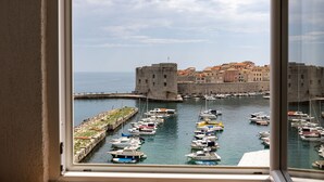 Un port où sont amarrés des bateaux, un château en arrière-plan et un ciel dégagé.