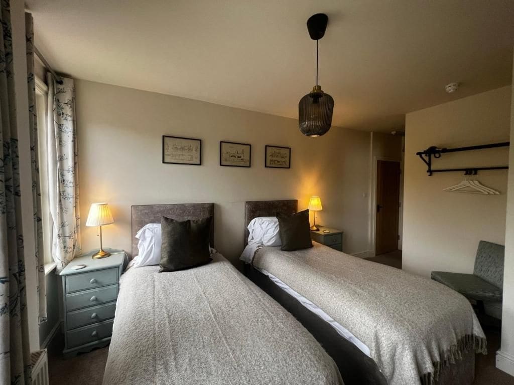 Quarto de hotel com duas camas, luminárias de cabeceira, guarda-roupa e quadros na parede.
