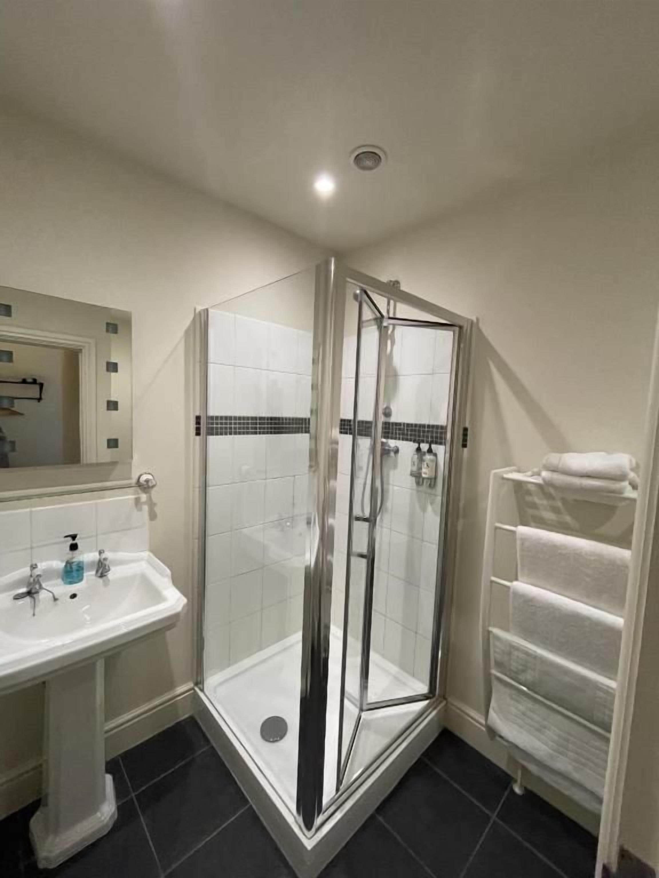 A bathroom with a glass-enclosed shower, a pedestal sink, and a towel rack.