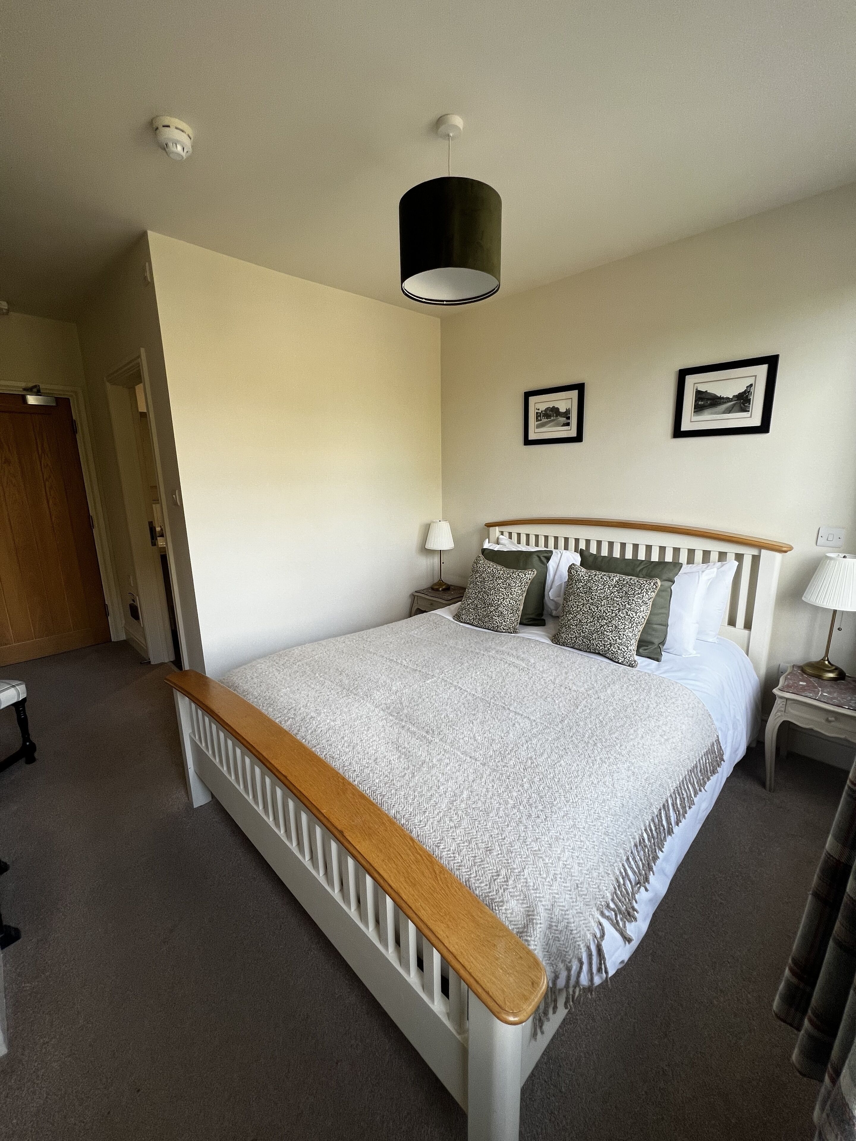 A bedroom with a single bed, a bedside table with a lamp, and a door leading to another room.