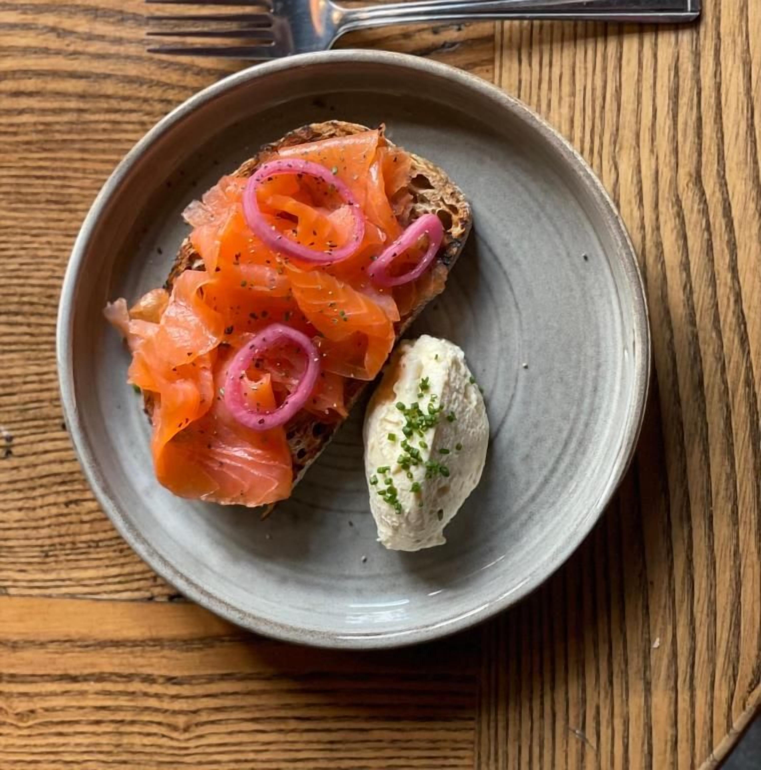 A plate with a slice of bread topped with smoked salmon and red onion, accompanied by a dollop of cream cheese.