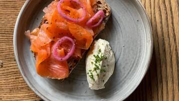 A plate with a slice of bread topped with smoked salmon and red onion, accompanied by a dollop of cream cheese.