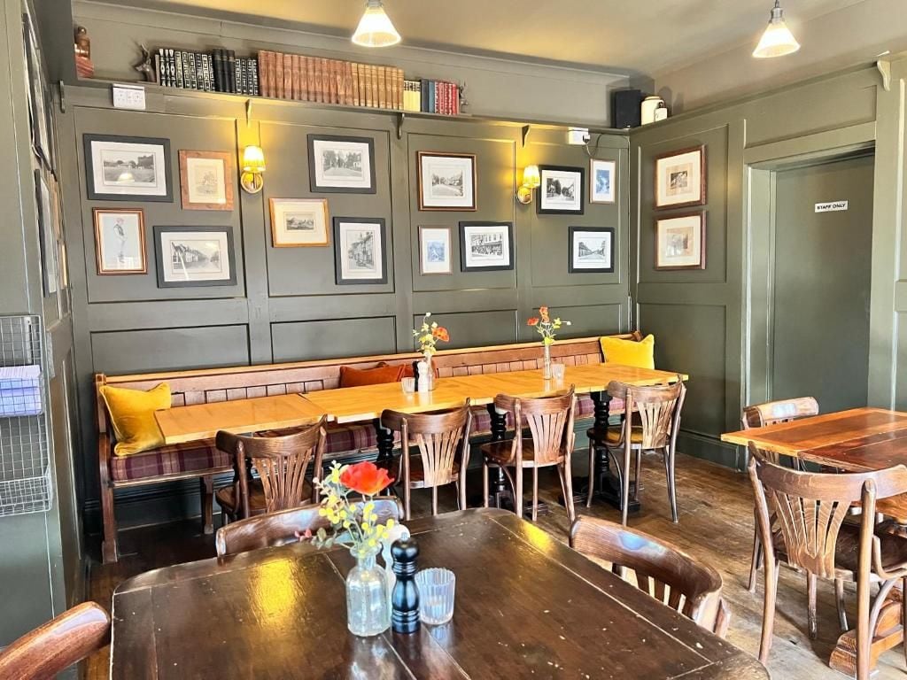 A dining area with a long wooden table, multiple chairs, a bench, and framed pictures on the wall.