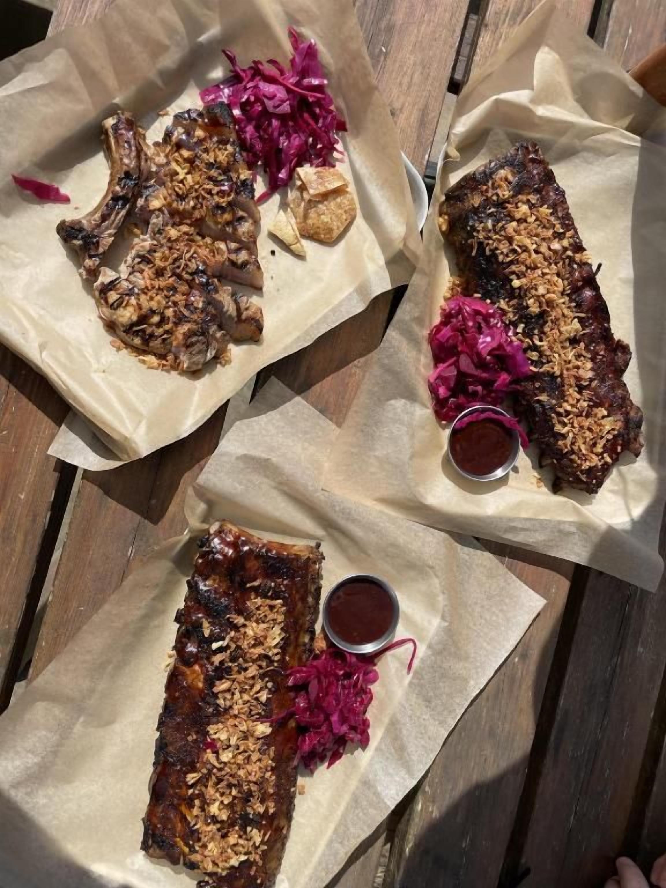 A wooden table with three plates of food, each with a different type of meat and a side of red cabbage.