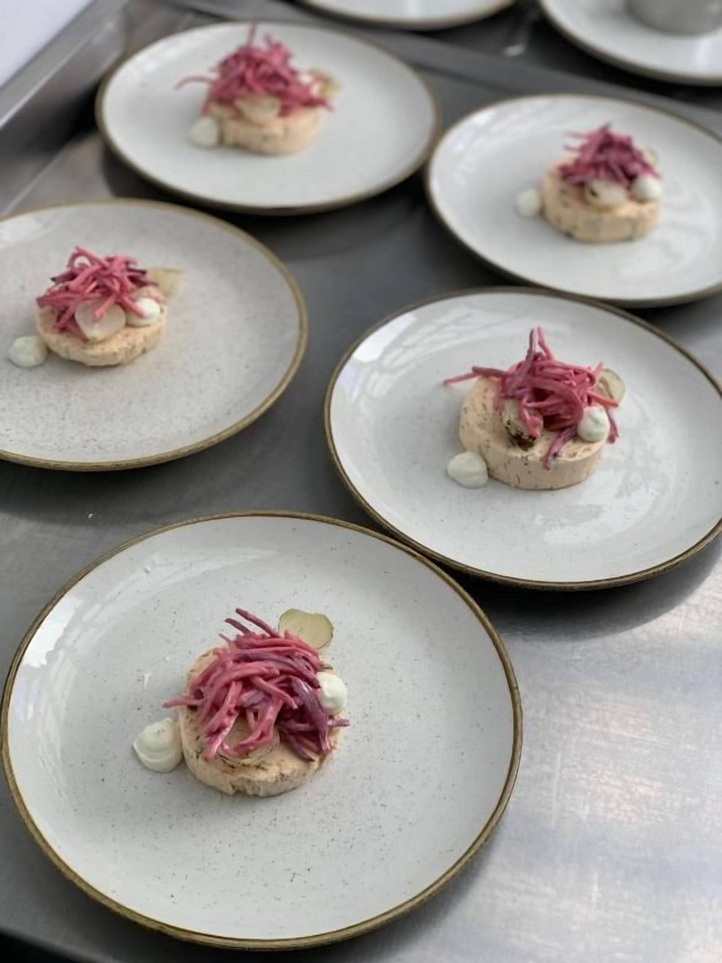 A tray with four plates of food, each with a central mound and garnished with pink and white elements.