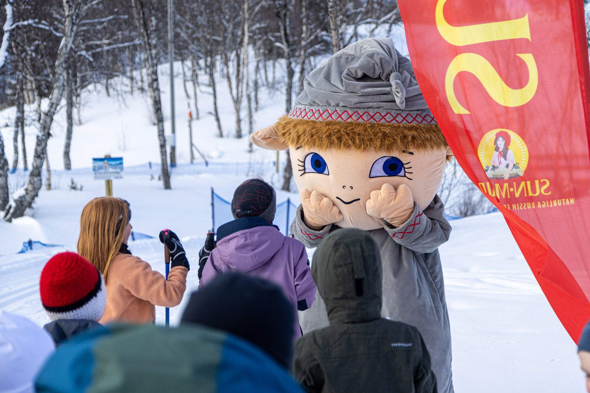 A mascot in a snowy outdoor setting with people in the background.