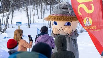 A mascot in a snowy outdoor setting with people in the background.