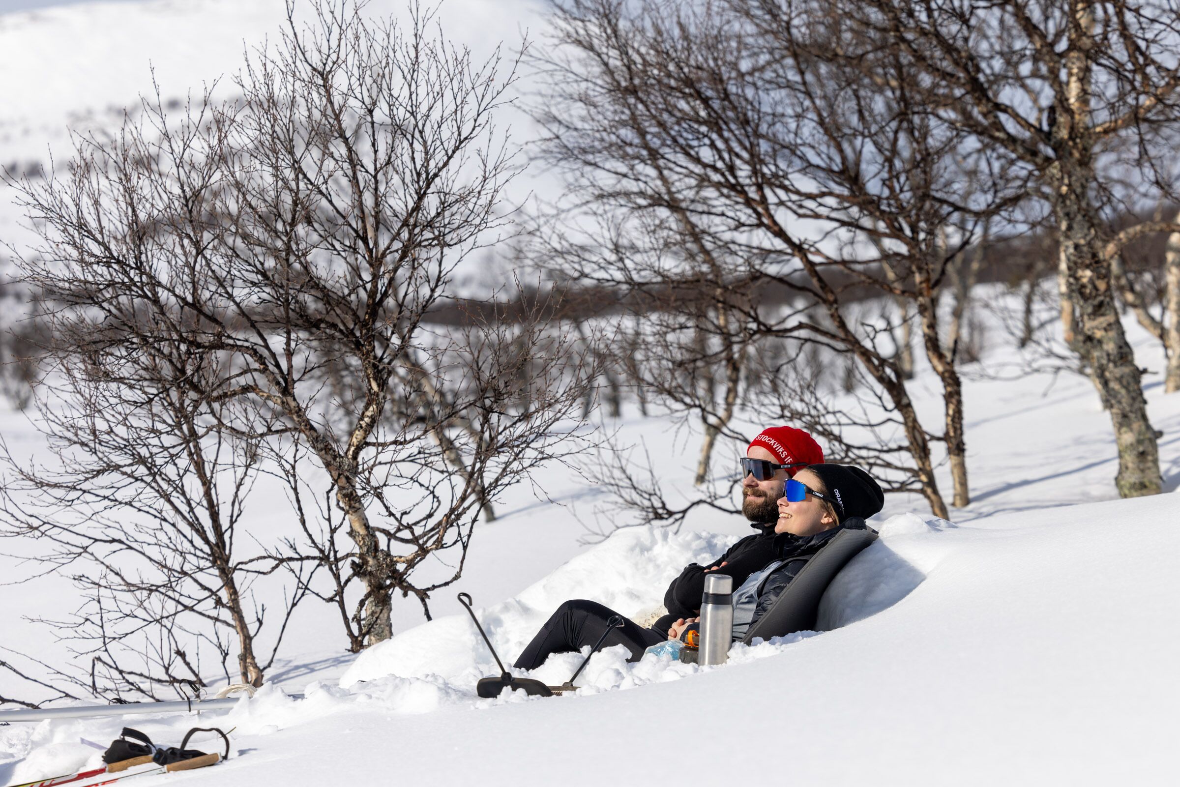 A person lying on a sled in a snowy landscape with bare trees.