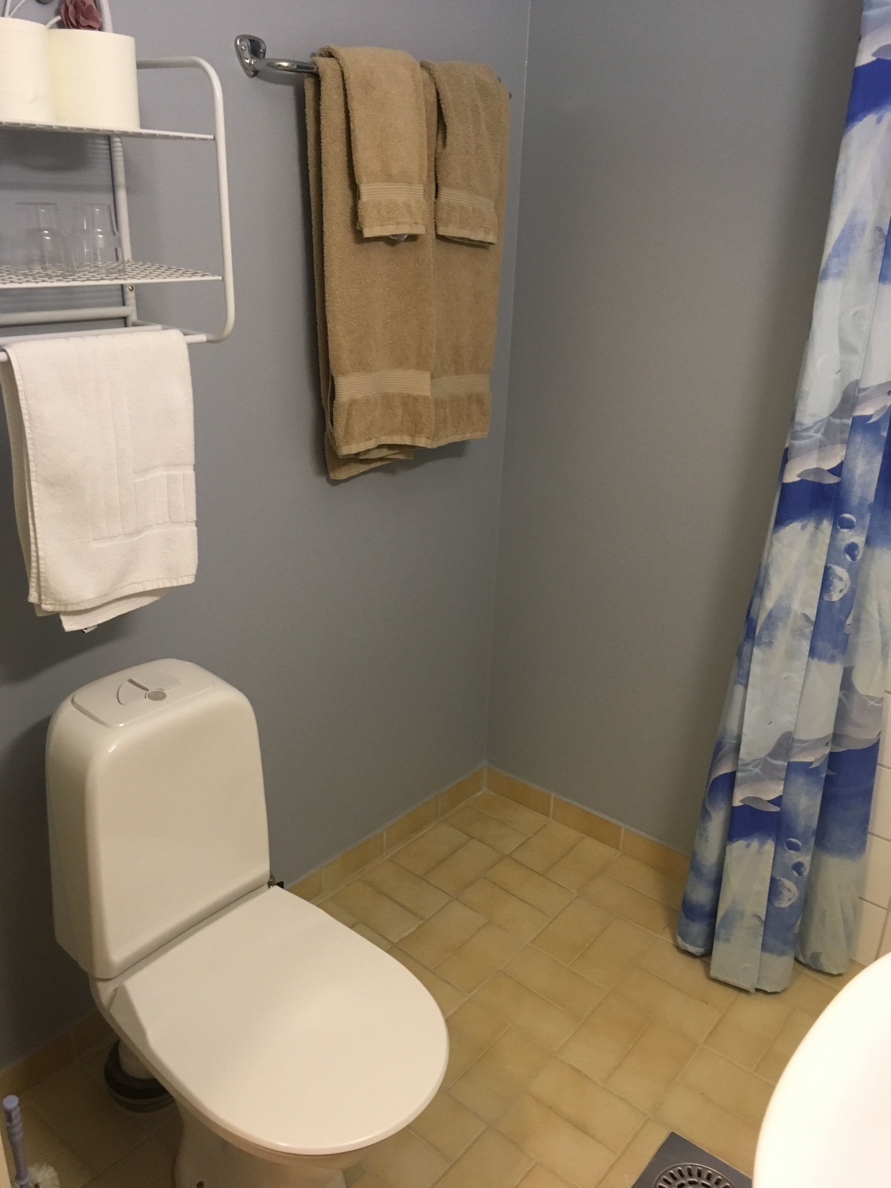 A small bathroom with a toilet, a shelf with glasses, and towels hanging on a rack.