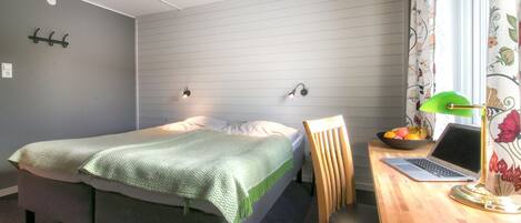 A bedroom with a bed, a desk with a laptop, a chair, a lamp, and a fruit bowl.