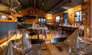 A restaurant with wooden interiors, tables set for dining, and a bar area with glasses and bottles. - Hotell Bruksvallsliden (Bruksvallarna)