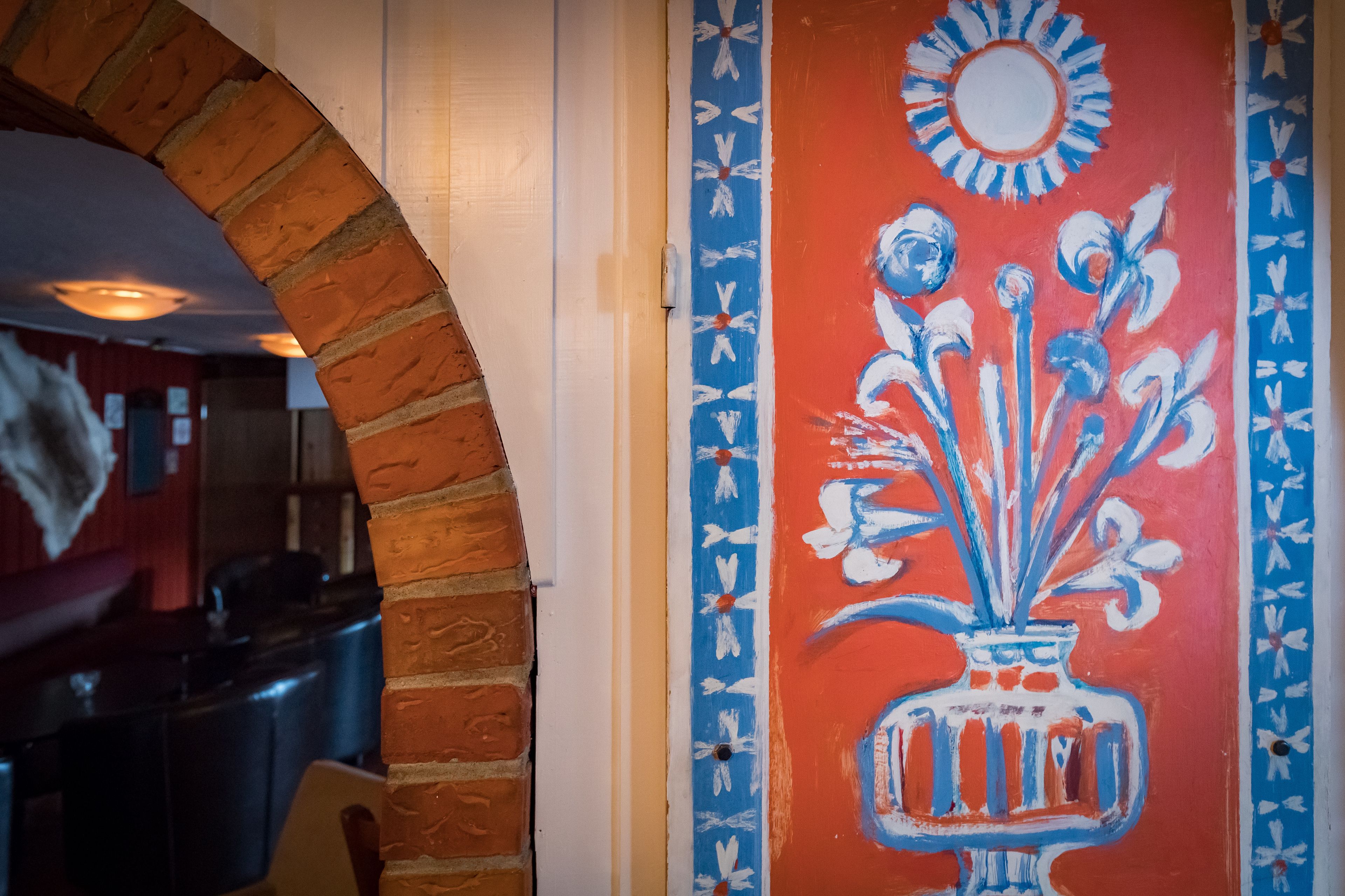 A room with a brick archway, a red wall with a blue and white floral pattern, and a white door.