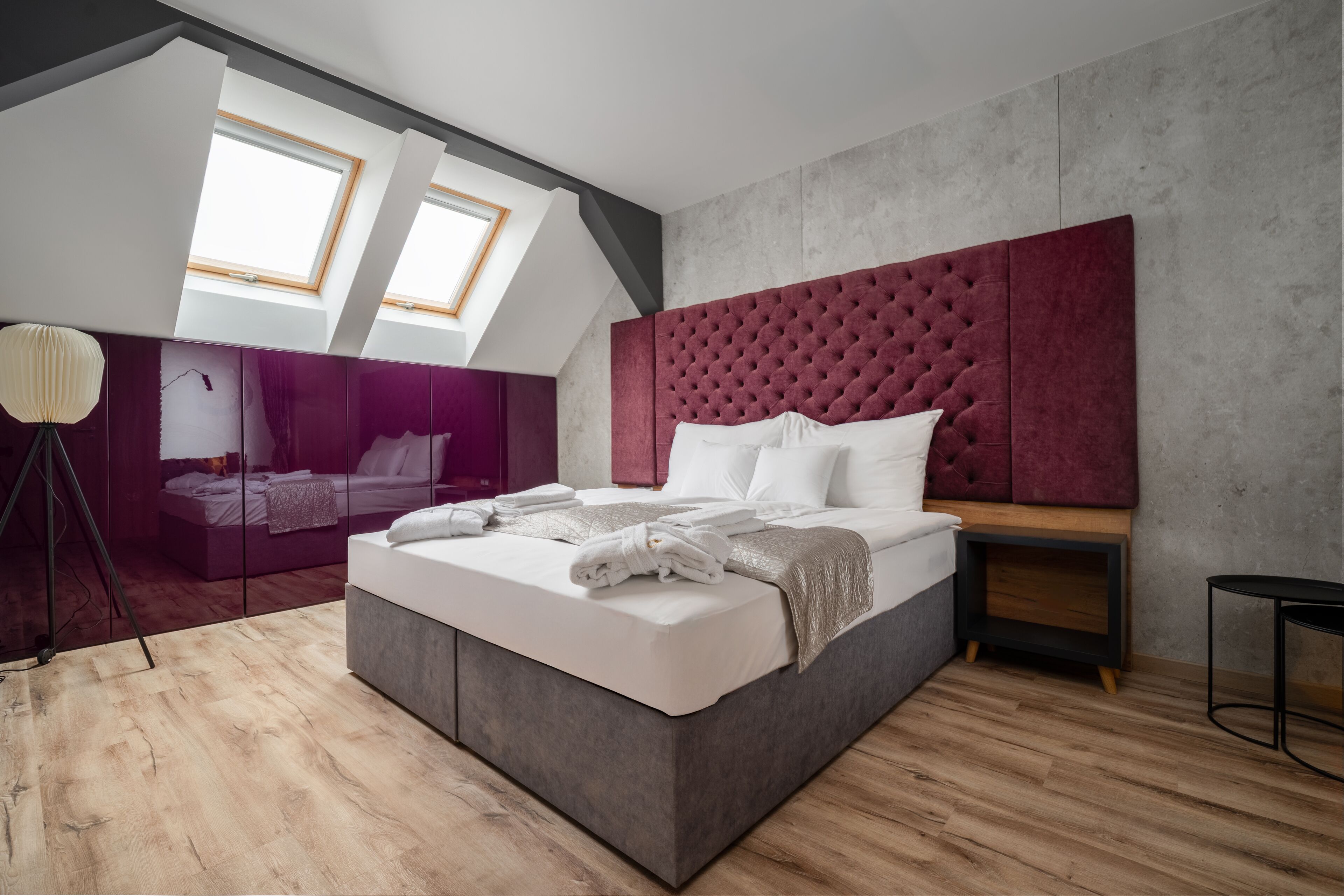 Un dormitorio moderno con una cama grande, un cabecero tapizado en rojo y un tragaluz.