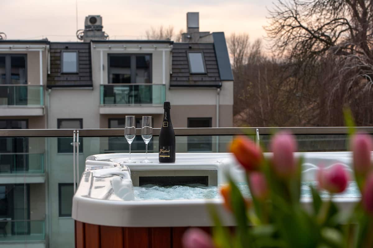 A hot tub with a bottle and glasses on a balcony overlooking a residential area.