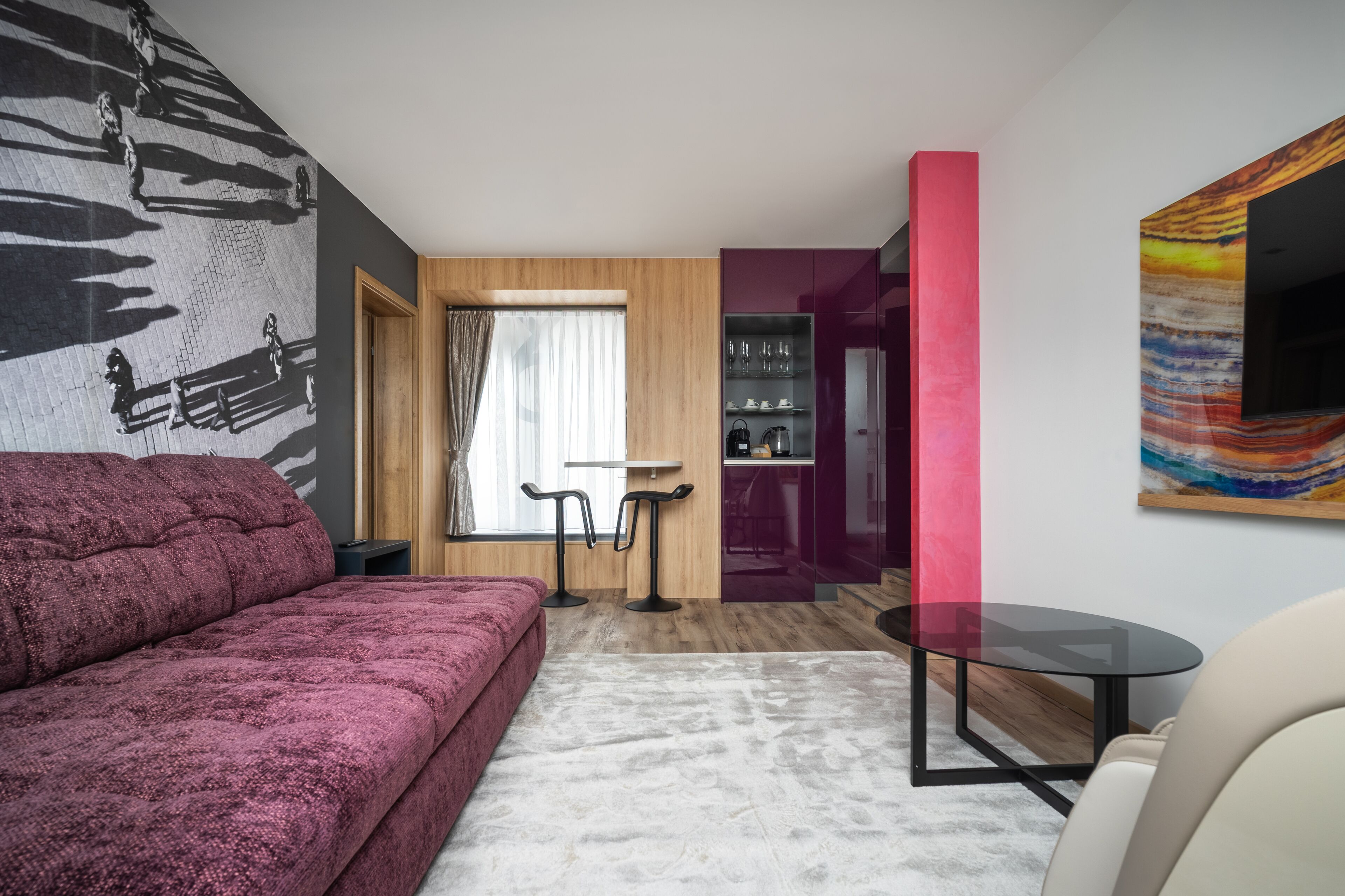 A modern living room with a red sofa, a glass table, and a TV mounted on a wall with a colorful abstract painting.