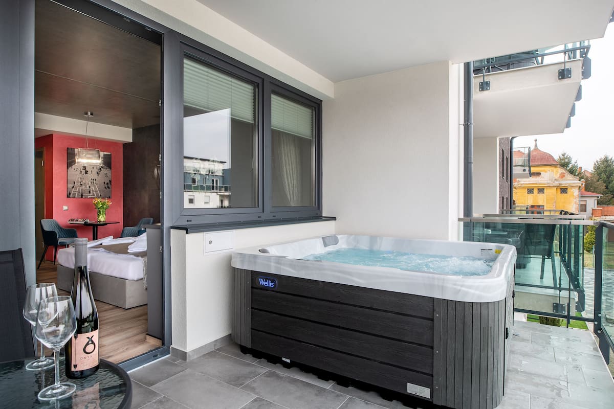 A modern hotel room with a hot tub, a dining area, and a balcony with a glass railing.