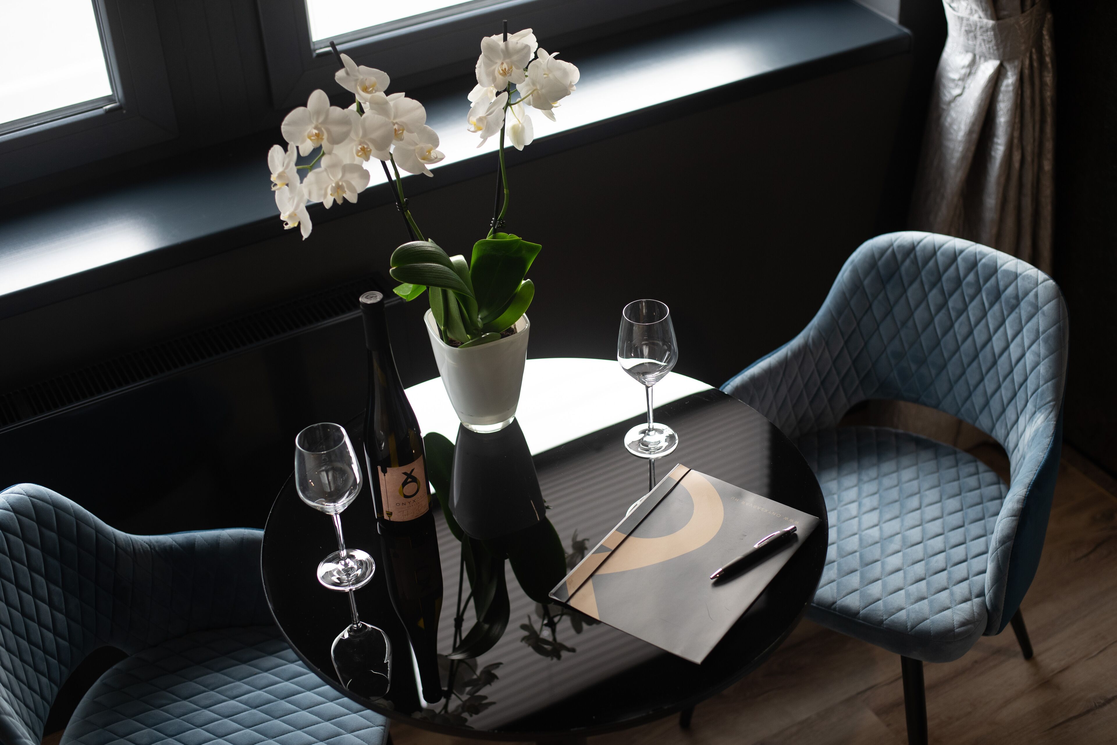 Una mesa de comedor con dos sillas, un jarrón con orquídeas blancas y dos copas de vino.