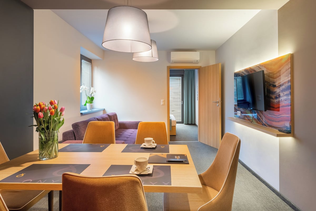 A modern hotel room with a dining area featuring a wooden table, orange chairs, and a vase of tulips.