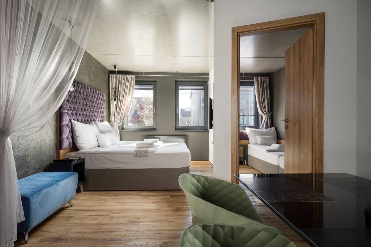 A modern bedroom with a large bed, a blue bench, a green chair, and a wooden door.