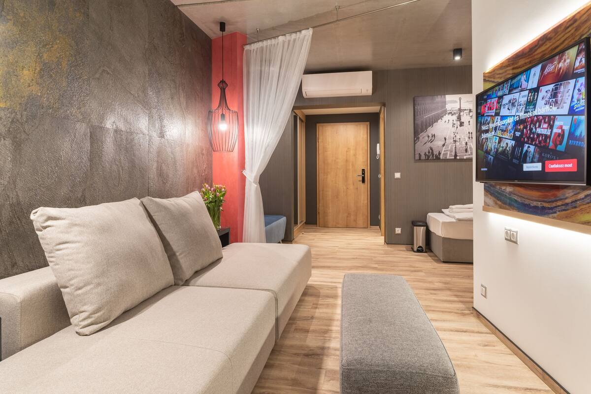 A modern living room with a sofa, a bench, a wall-mounted TV, and a wooden door.