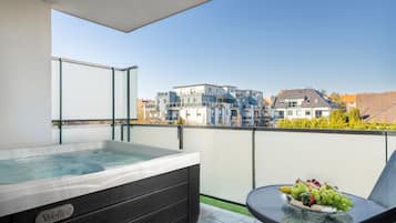 A balcony with a hot tub, a table with fruit, and a view of residential buildings.