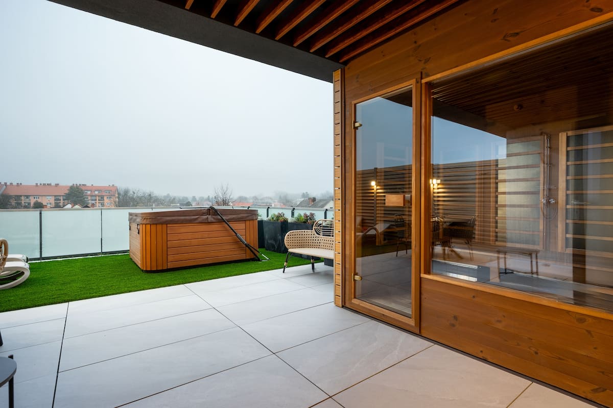 A modern outdoor patio with a hot tub, a wooden deck, and a glass door leading to an interior space.