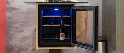 A wine refrigerator with a wine bottle inside, a coffee machine, and two cups on top.