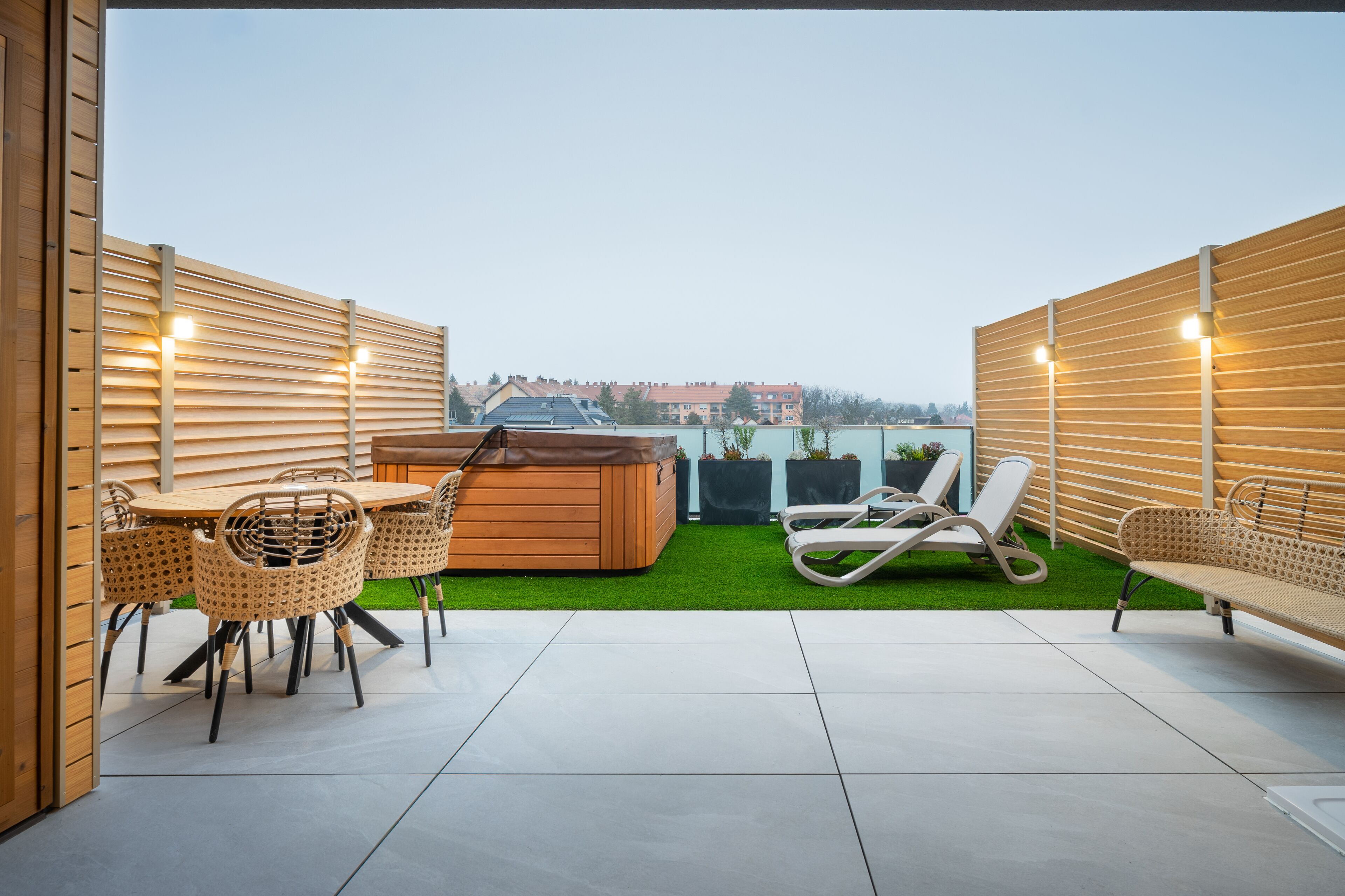 A rooftop patio with a wooden table and chairs, a hot tub, and a lounge chair.