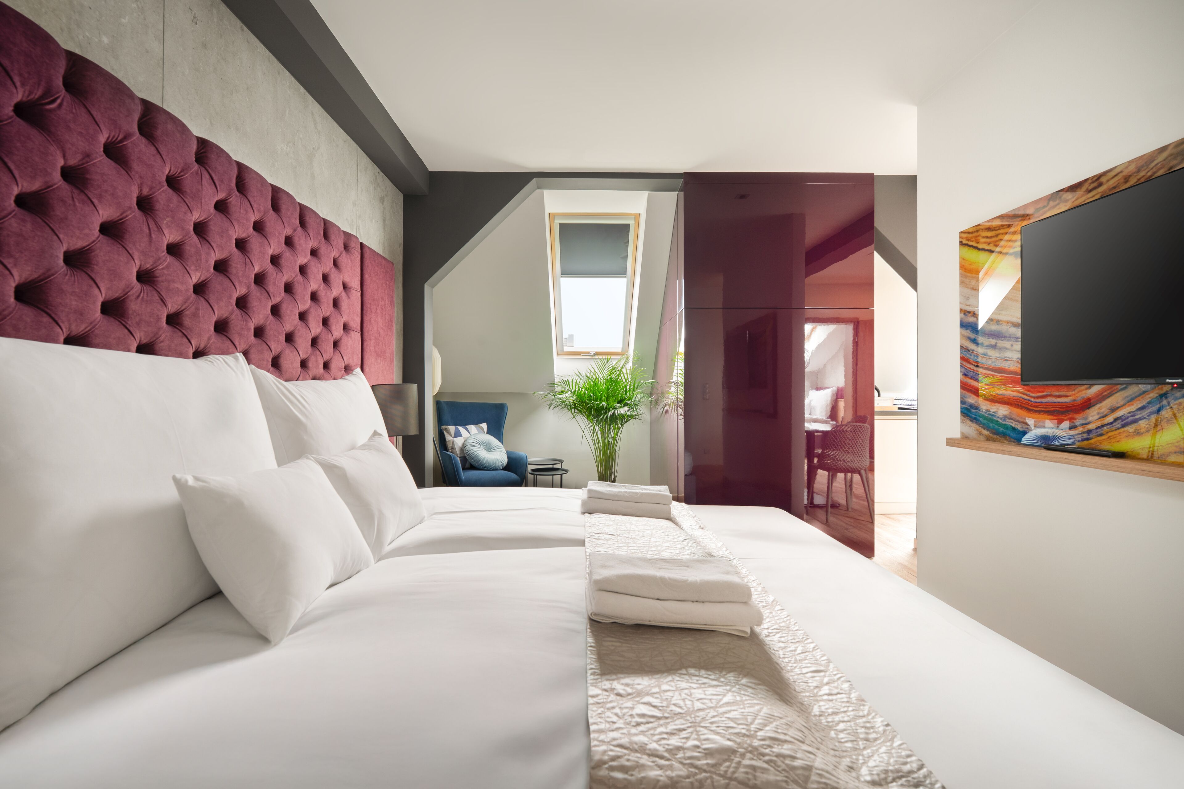 Une chambre d’hôtel moderne avec un grand lit, une tête de lit capitonnée, un téléviseur à écran plat et un tableau au mur.