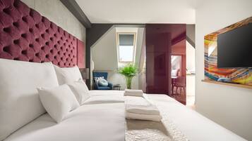 Une chambre d’hôtel moderne avec un grand lit, une tête de lit capitonnée, un téléviseur à écran plat et un tableau au mur.