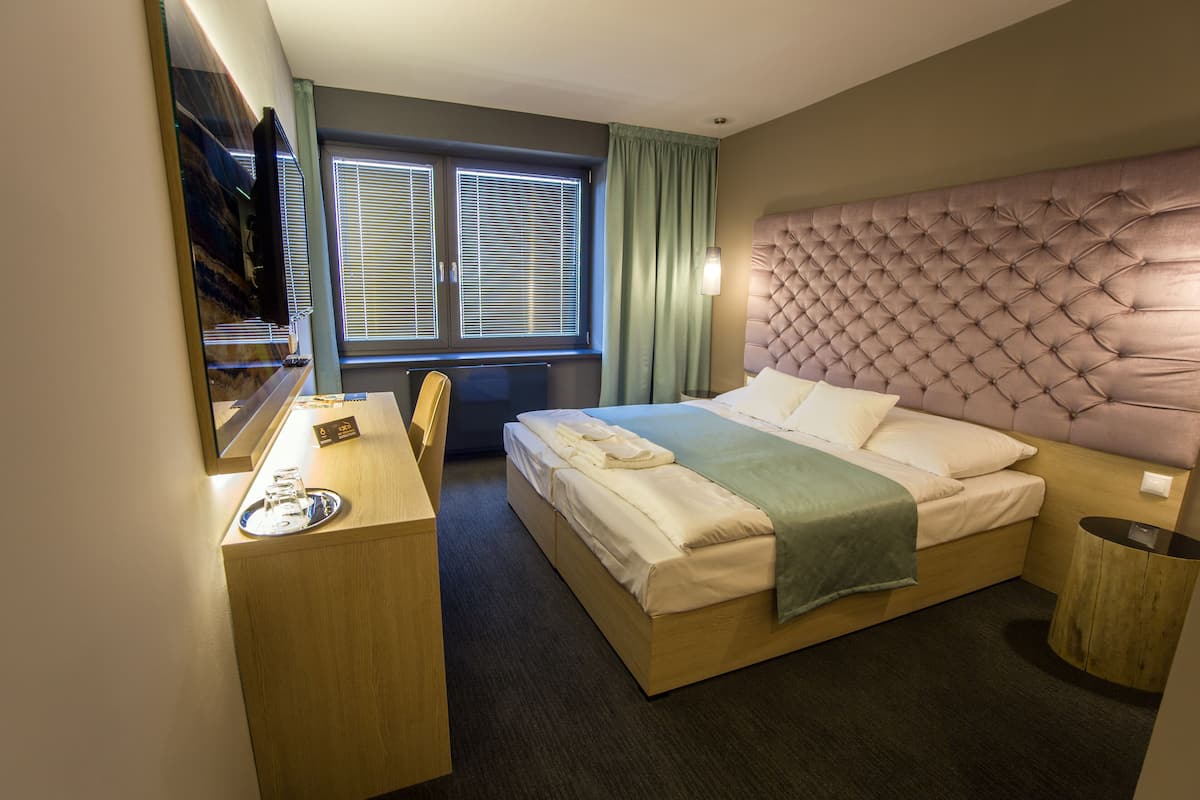 A hotel room with a bed, a desk, a chair, a television, and a window with blinds.