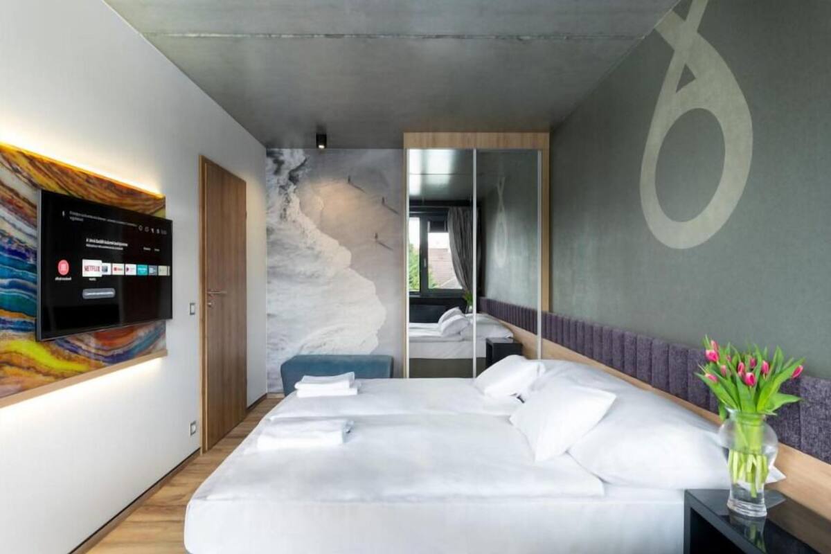 A modern hotel room with a large bed, a flat-screen TV mounted on the wall, and a large abstract painting.